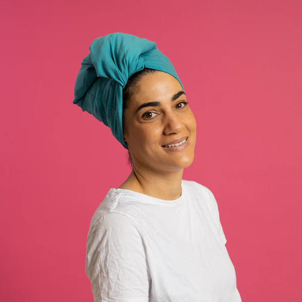 Woman wearing teal silk lined tubular hair wrap (silk lined buff) with pink background