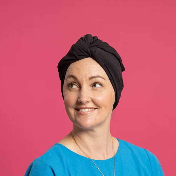 Woman wearing black Silk Lined Tubular Hair Wrap (Silk Buff) in black against pink background. 