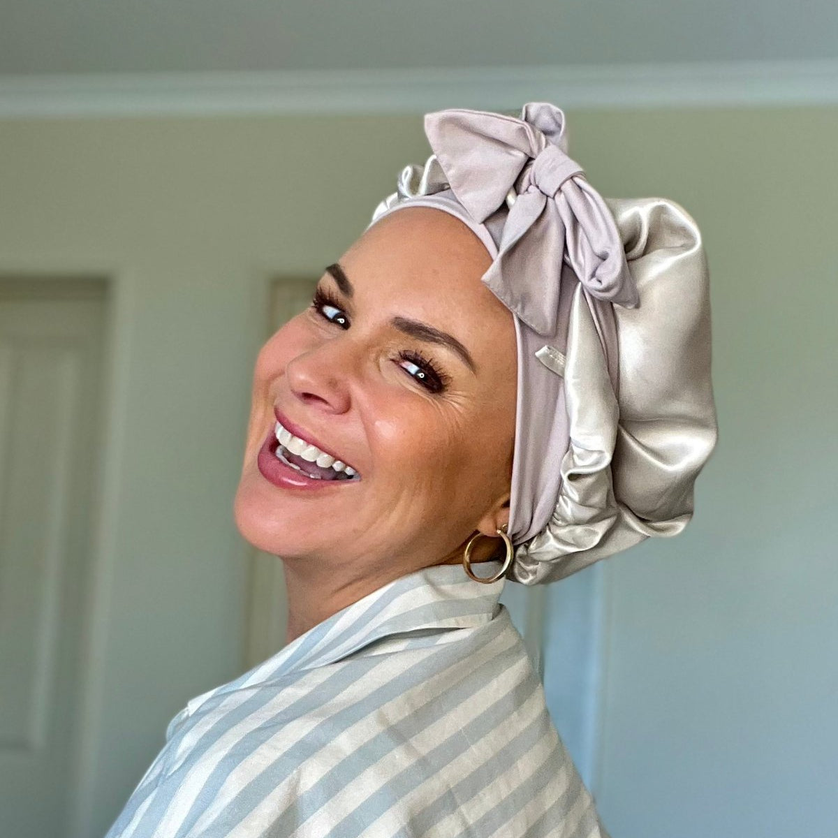 Woman wearing a silk hair cloud bonnet to protect curls and striped robe indoors.
