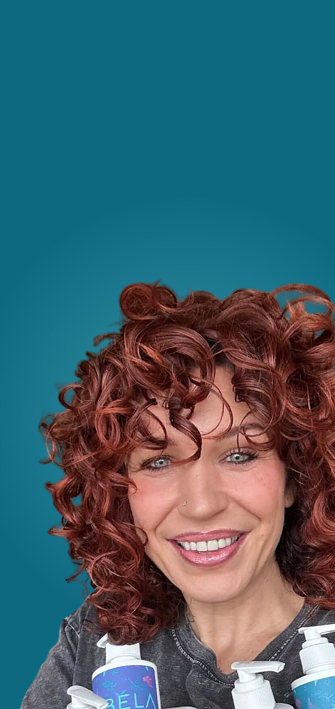Smiling woman with bouncy, defined red curls holding Cabela curl care products