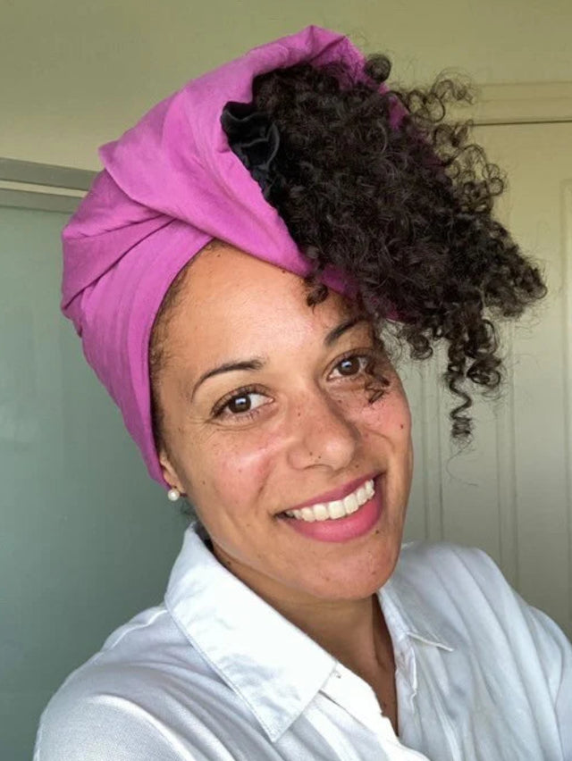 Woman wearing a pink headscarf and white shirt indoors