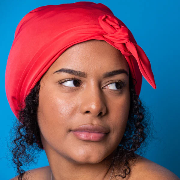 Close up, curly haired woman wearing soft red Shower Cap against blue background 